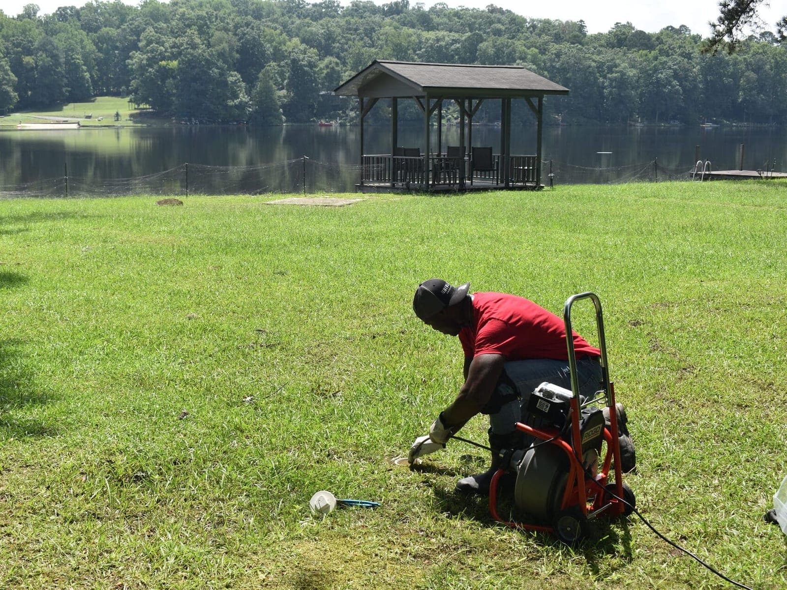 A-Team Plumbing technician running a drain machine at an outdoor cleanout beside a lake