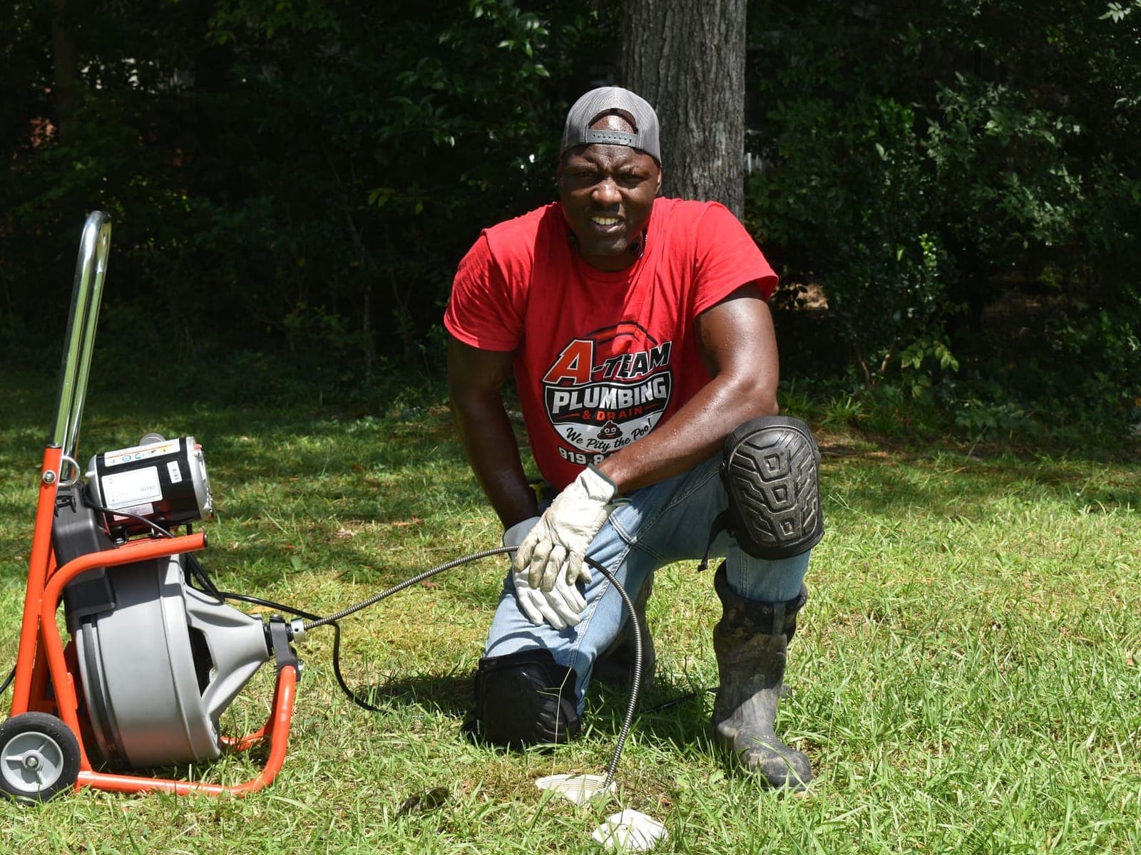 A-Team Plumbing technician kneeling beside a drain cleaning machine on a Durham job
