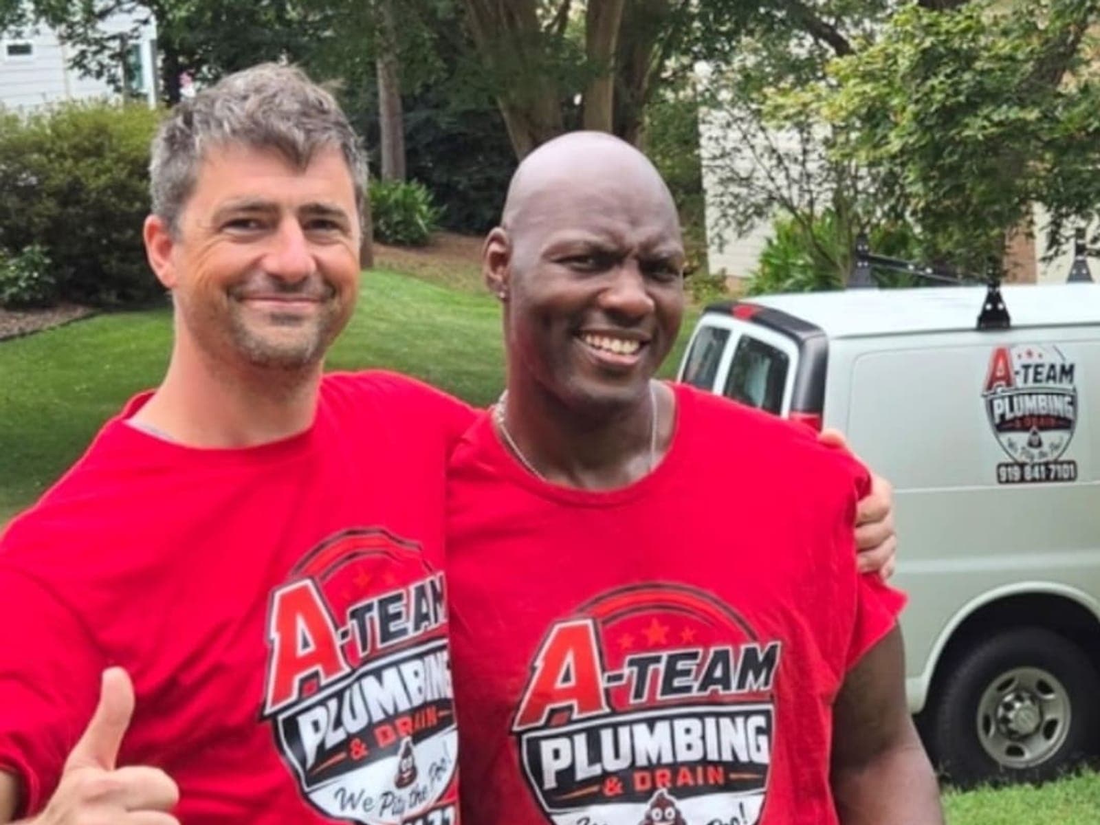 Two A-Team Plumbing & Drain technicians in branded red shirts standing together in front of the company van