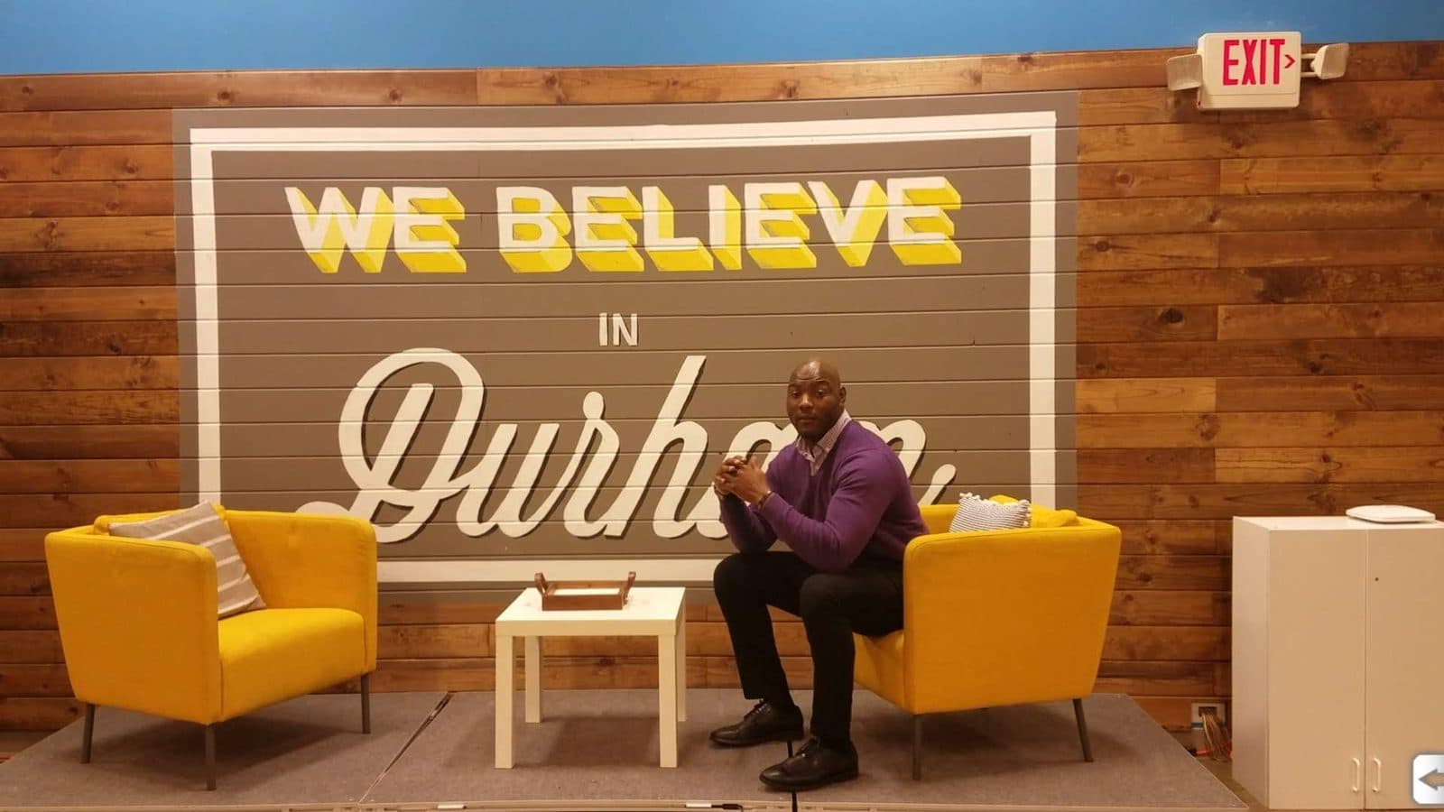 Anthony, founder of A-Team Plumbing & Drain, seated in front of a “We Believe in Durham” mural